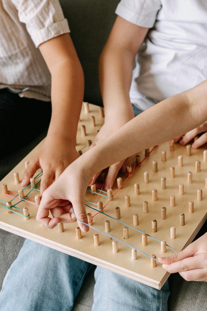 Children enjoy a mindful activity with a wooden geoboard, using colorful rubber bands.